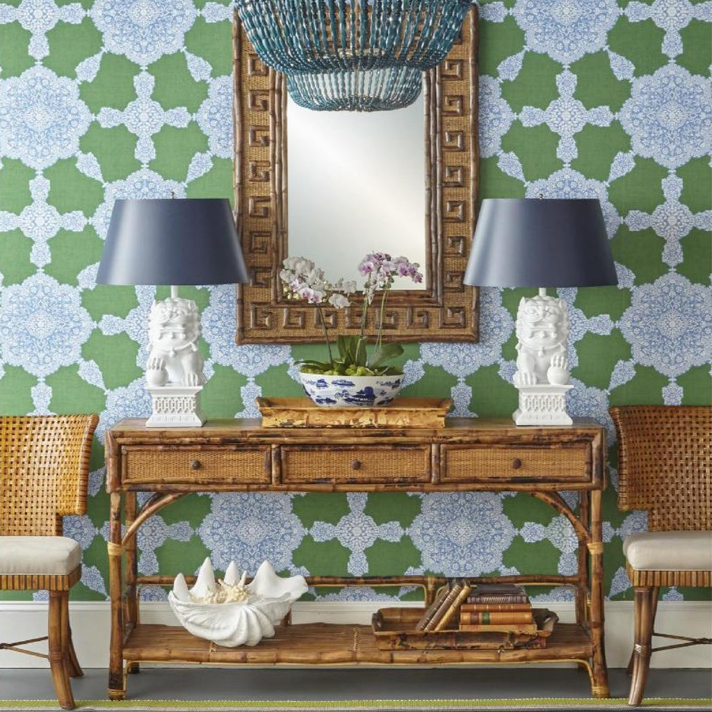 Bamboo console table with lamps and mirror against a patterned green wallpaper backdrop.