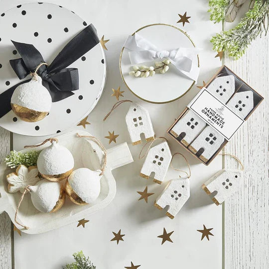 Holiday decorations with white and gold baubles, house ornaments, and gift boxes on a star-patterned surface.