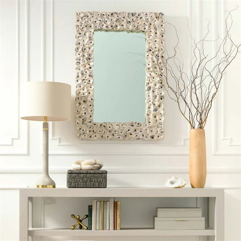 Elegant room decor with a textured mirror, lamp, vase with branches, books, and decorative objects on a shelf.