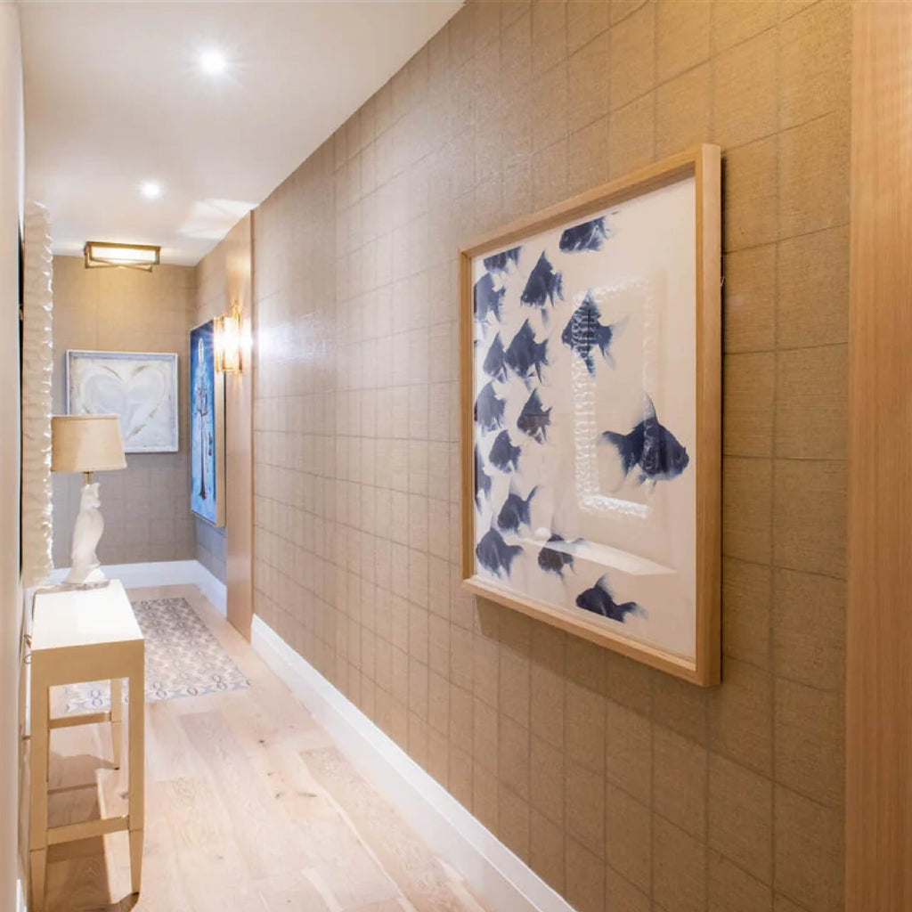 Hallway with beige walls, framed art, a small table with a lamp on the left, and a patterned rug on the floor.