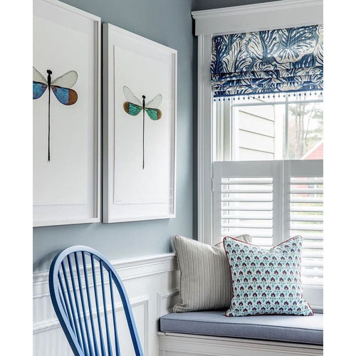 A cozy nook features a blue chair, dragonfly wall art, and a patterned cushion on a bench beside a window with blinds and a blue shade. The Damselfly Turquoise Photography Art by Barloga Studios adds charm to the space, enhancing your art collection with unique framing options.