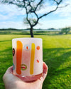 Holding an Abigails White + Multi-Color Cocktail Tumbler set against a sunny backdrop of trees and lush green fields.