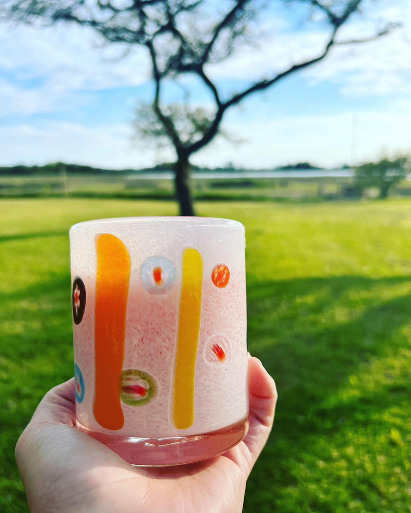 Holding an Abigails White + Multi-Color Cocktail Tumbler set against a sunny backdrop of trees and lush green fields.