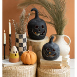 Assorted Halloween decor featuring Black Clay Jack-O-Lanterns by Kalalou, a small pumpkin, candles, and vases arranged on woven baskets and wooden stools.