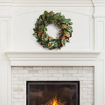 A Grand Magnolia Leaf Wreath from Napa Home & Garden hangs above a white brick fireplace with a burning fire in the hearth, perfect for interior use.