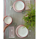 Top view of a dining table setting with Always Relish Simple Round Red Rim Melamine Dinner Plates (set of 4), striped napkins, silverware, and a greenery centerpiece.