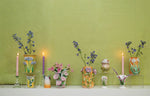 Handmade Mango with Lavender Flower Vase by Abigails and lit candles on a shelf against a textured green wall.