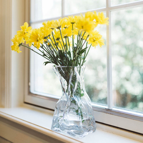 Abigails' Le Sack Large Glass Vase with yellow flowers catches light on a windowsill against a blurred outdoor background.