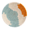 The Spark Art Plate Medium Set by Kazi Goods features round, handmade art pieces crafted from natural fibers, displaying a stunning spiral pattern in teal, cream, and orange sections, perfect for doubling as exquisite woven wall art.