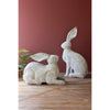 The Kalalou Rustic Metal Rabbits set of 2 rests on a wooden floor against a vibrant red wall.