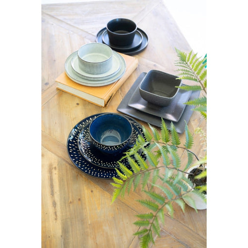 Glacier Ceramic Dinner Collection by Kalalou on a wooden table with books and a fern plant.