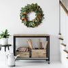 Entryway with a Grand Magnolia Leaf Wreath by Napa Home & Garden on the wall, console table with storage boxes and rolled paper, potted plant on a stool, and a metal pitcher on the floor.