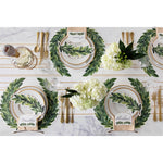 An elegant table setting featuring greenery-themed plates, gold cutlery, wine, and white hydrangea centerpieces is enhanced by the natural touch of Hester & Cook's Wreath Paper Placemats Die Cut.