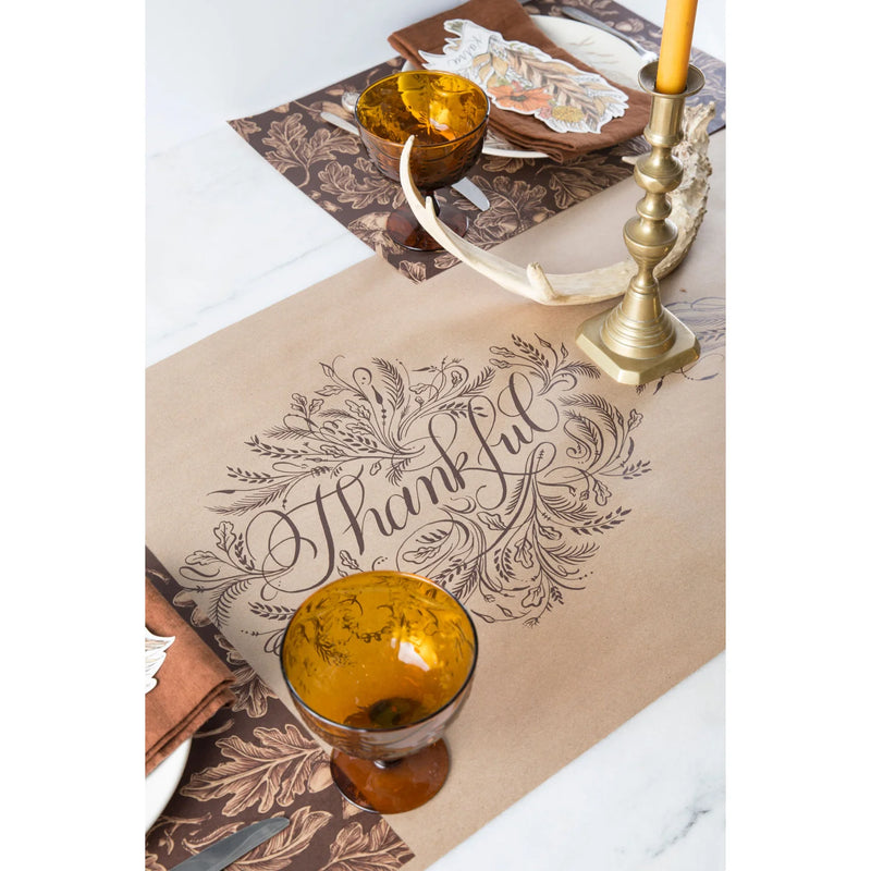 Table setting with a "Thankful" placemat, amber goblets, antler decor, and the Thankful Paper Table Runner by Hester & Cook featuring a thankful message crafted on natural paper.