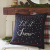 A Taylor Linens "Let It Snow" Linen Pillow, featuring embroidered snowflakes, white dots, and red trim, is elegantly placed on a plaid cushion next to a rustic mantel.