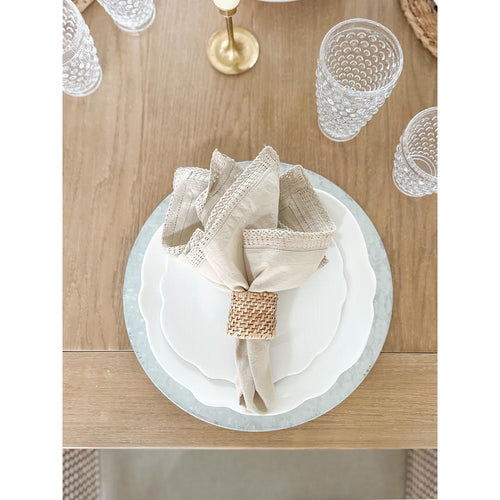 Elegant table setting with a BPA-free woven napkin holder, layered Always Relish Scalloped White Melamine Dinner Plates (set of 4), textured glasses, and a wooden table.