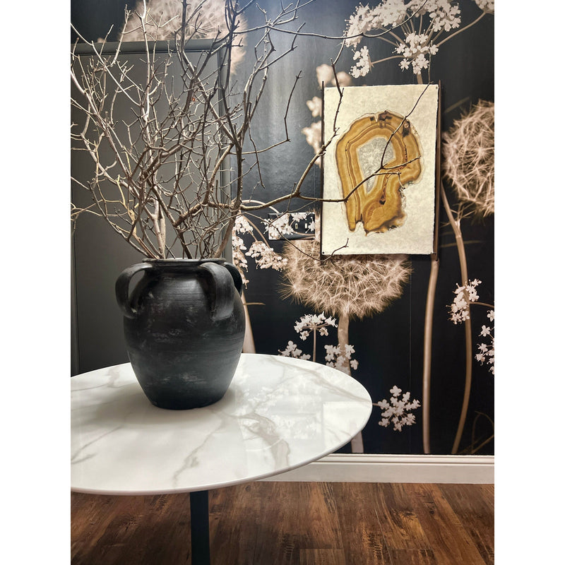 An Amber Agate 1 Photography Art print by Barloga Studios hangs on a floral-patterned wall, complementing the round marble table with a vase of bare branches, and accented by archival wood frames.