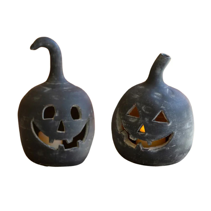 The set of two Black Clay Jack-O-Lanterns by Kalalou, each with a unique stem shape and a glowing interior, evoke the feel of smiling jack-o-lanterns.