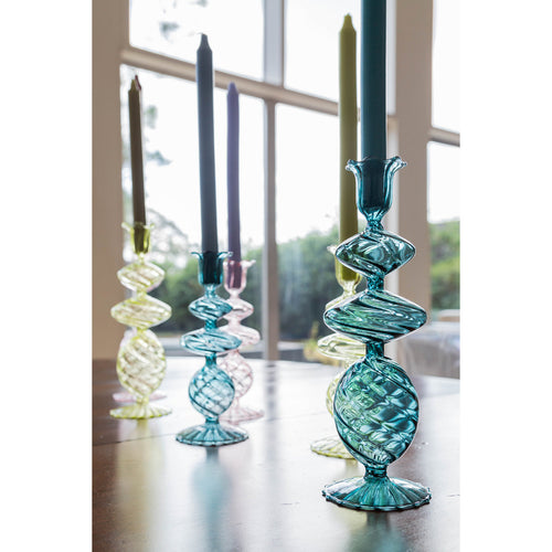 Abigails Blue Swirl Glass Candlesticks stand on a table by a large window in a sunlit room, holding retro-inspired aqua blue taper candles.