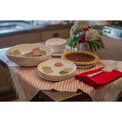 A pecan pie, plates, and Always Relish Christmas Ornaments Melamine Serving Bowls filled with flowers adorn a table covered with a red and white striped cloth, perfect for a Christmas gathering.